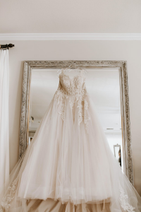 A wedding gown hanging in front of a mirror.