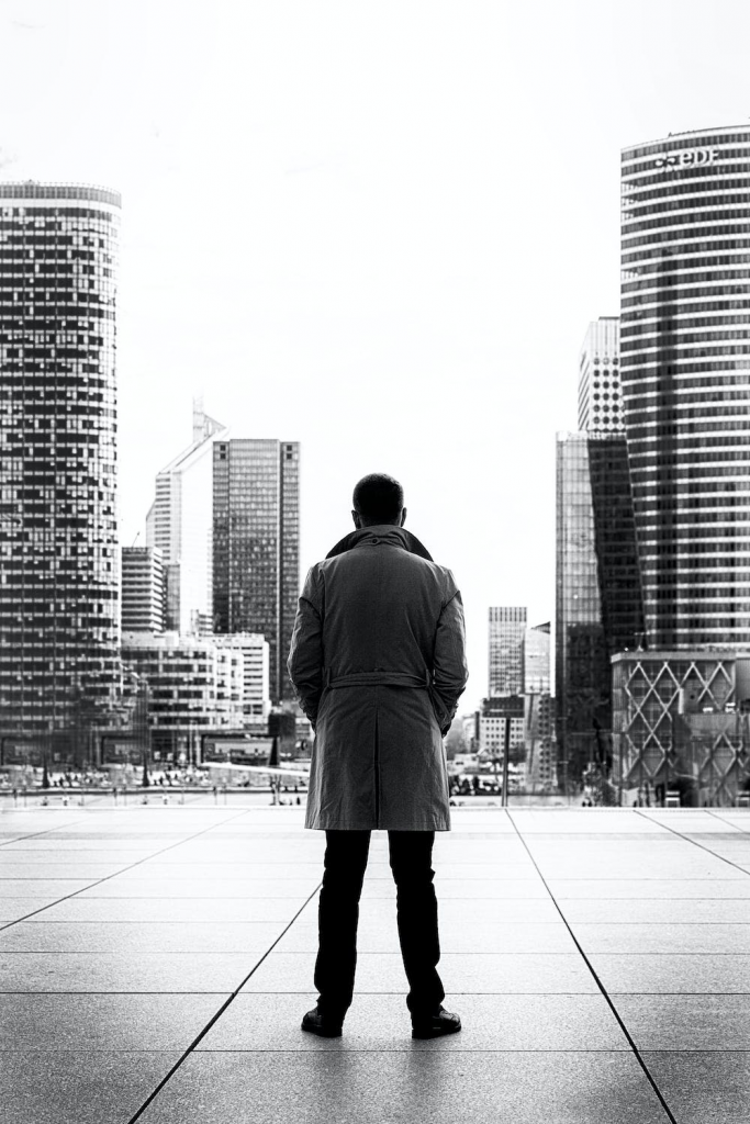 A black and white photo of a man looking out at the city wearing a coat.
