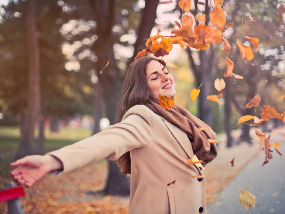 A woman wears her coat while standing outdoors during the fall.