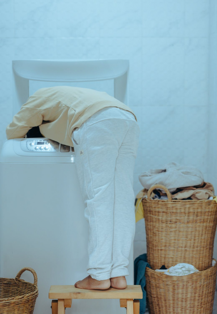 A person stands on a stool while unloading a large washing machine.